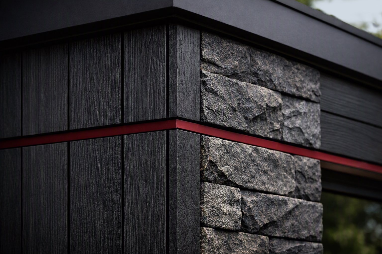 Close-up of an exterior corner where dark vertical timber cladding meets split-face stone, with a burgundy line set into the joint and wrapping the corner beneath a black roof edge.